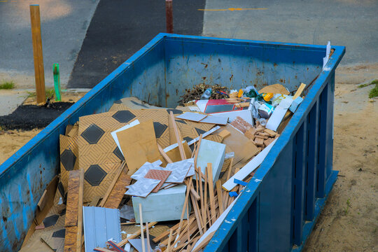 Construction debris fills large blue waste dumpster near street