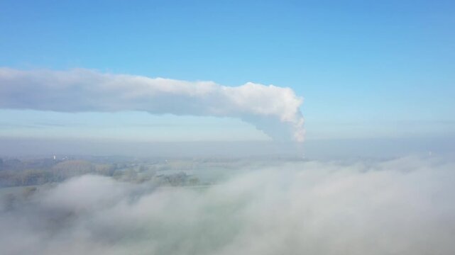 Drone shot of steam rising from the Dampierre nuclear power plant, surrounded by morning fog and a clear blue sky in France.