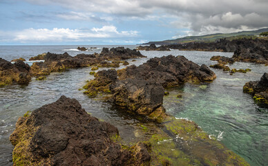 Natural volcanic swimming pools at Biscoitos on Terceira Island, Azores, Portugal, with ocean ladder, rugged lava rocks, Atlantic waves, and dramatic coastal scenery under a blue sky