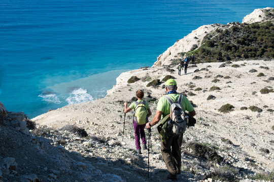 Hikers walking coastal trail above turquoise sea. People trekking coastline.
