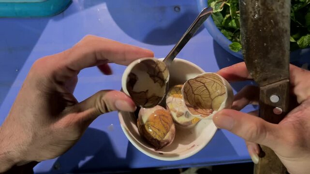 Detailed view of a man cracking and opening a boiled fertilized duck embryo, a traditional vietnamese delicacy known as balut