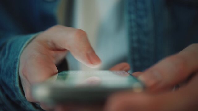 Close-up macro male hand in blue denim shirt typing on smartphone. Daylight indoors. Fingers interacting with touchscreen writing message. Mobile communication, online chat and digital lifestyle