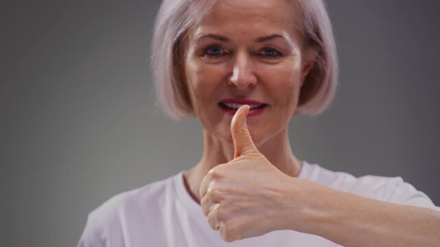 Like portrait: senior elderly mature woman, 60-80s, giving thumbs up hand gesture sign, smiling. Old female shows a like with her hand or palm. Good great news, positive feedback.