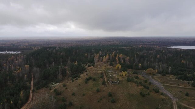 Aerial view of Dretunsky range shows ruined bunkers on a hill, two lakes, autumn birch and pine, dirt roads, a lone vehicle, small figures, and crisscrossing tracks.