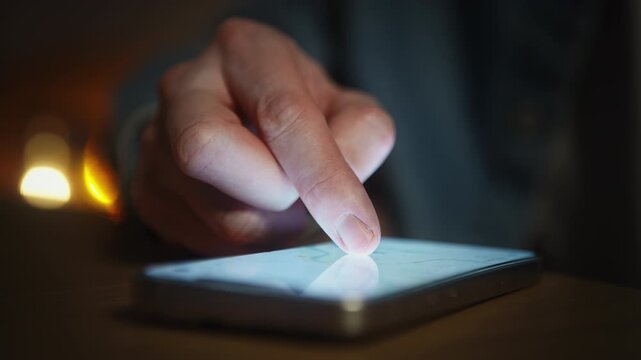 Close-up of man in blue denim shirt using smartphone map app, low light indoors scene. Pinching and zooming on touchscreen while searching location. Navigation, route planning and mobile technology
