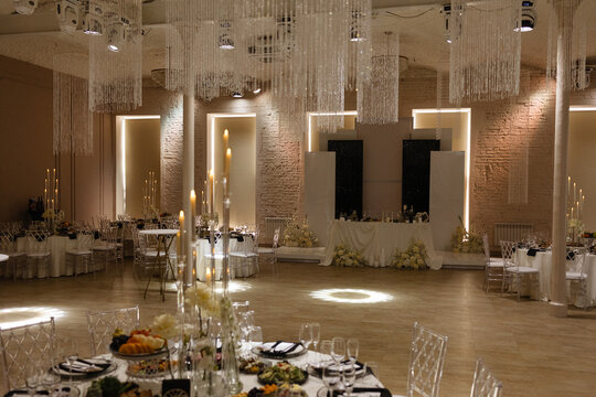 Elegant wedding banquet hall with decorated tables, floral arrangements, candles and crystal chandeliers. Classic interior with light brick walls and wooden floor for ceremony,reception, luxury event.