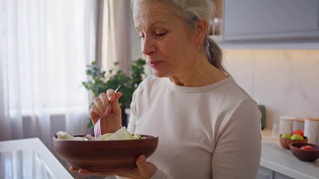 Senior lady eats tasty salad with cucumbers and lettuce at home