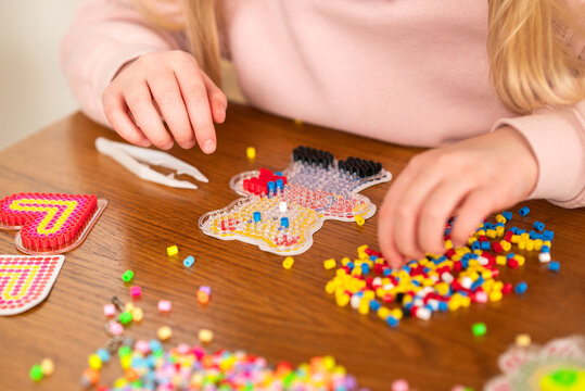Child's hands creating a bear pattern with colorful fuse beads on a wooden table. Creative DIY craft at home. Thermo mosaic, ironing beads, fuse beads