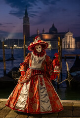 Obraz premium Masked woman in ornate orange jester costume, and holding a little lookalike jester doll, poses for the camera at San Marco, at the annual Venice Carnival.