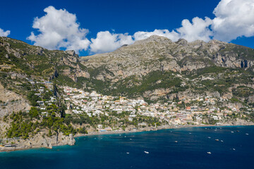 Obraz premium An expansive aerial perspective reveals the coastal village of Positano, Italy, nestled between steep limestone cliffs and the deep blue waters of the Amalfi Coast. The dramatic mountains rise above