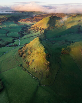 Aerial view of the stark, shadowed edges of Mam Tor contrast against the vibrant green fields, creating a tapestry of light and shadow, Chrome Hill, Peak District National Park, United Kingdom.