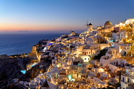 Santorini's Oia village, illuminated at dusk, overlooking the sea.