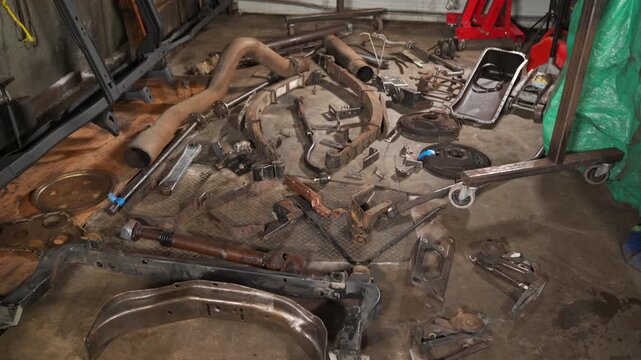 Large quantity of car parts of all sizes laying on the stained garage floor. 