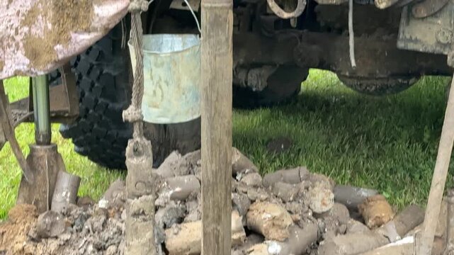 Drilling rig extracting soil cores in grassy field, truck mounted rotary rig creating borehole while driller operates controls, core tray with cylindrical samples laid on grass, geologist.
