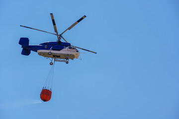 Firefighting helicopter filling water with bambi bucket from a lake