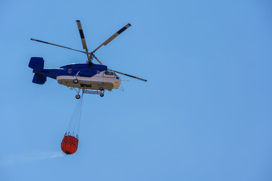 Firefighting helicopter filling water with bambi bucket from a lake