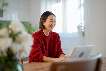 Japanese woman smiling, working on laptop at home