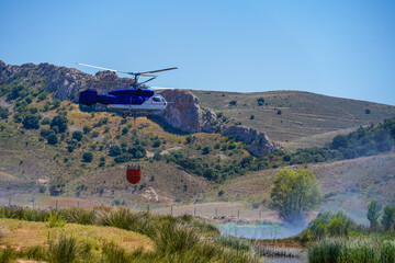 Fototapeta premium Firefighting helicopter filling water with bambi bucket from a lake