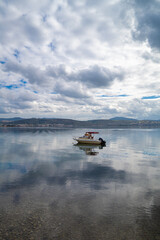 With calm, reflective sea and boats and cloudy sky