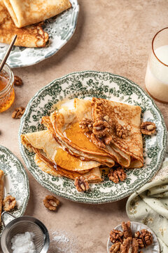 Delicious crepes served with nuts and honey folded on ceramic plate. Tasty morning breakfast on beige table background, Maslenitsa concept