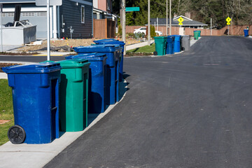 Residential garbage day, row of garbage and recycle rolling bins lined up at street curb on a sunny winter day
