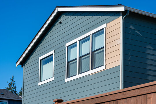 Newly built house with section of siding replacement, exterior wall with windows and blinds on a sunny winter blue sky day
