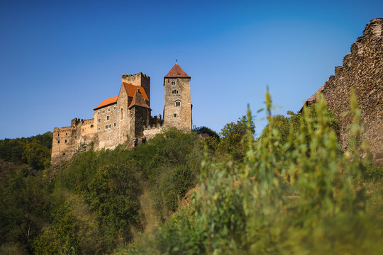 Scenic view of the medieval Hardegg Castle with stone towers and red roofs standing on a rocky hill in Austria under a blue sky.