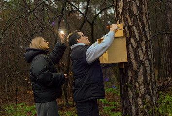 Naklejka premium A young man and woman hang a birdhouse on a tree