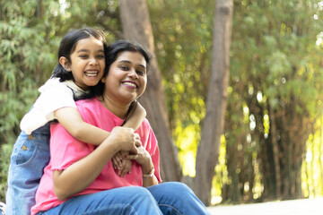 Indian happy mother and daughter embracing and hugging each other. Loving young mother holding her lovely daughter at park. cheerful daughter enjoying a ride on the back of her mother