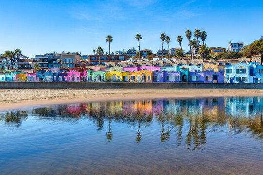 Colorful seaside houses of Capitola Village reflected in calm water on a sunny day. Vibrant coastal architecture, palm trees, and beach atmosphere along the California coast