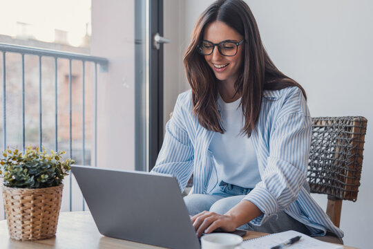 Successful virtual teamwork. Laughing gen z girl remote employee blended learning student communicate by videocall via notebook sit at table in cozy coworking space collaborate on online group project