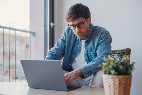 Young European businessman using laptop and technology apps for work or online learning, hispanic professional working at desk in office, focused on business tasks