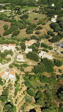 Drone shot of rural Pigna with traditional houses, lush greenery, and terraced fields. Mediterranean countryside scenery on a sunny day.