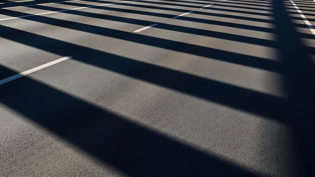 Shadows of buildings fall across an empty road with marked lanes on a sunny day