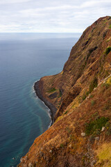 Fototapeta premium Madeira coastal cliffs. Steep rock formations descend into the Atlantic Ocean. High viewpoint of the rugged shoreline in Portugal.