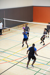 Adult male volleyball player in blue shirt performing forearm pass at gym court with volleyball