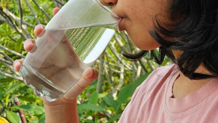 Fototapeta premium East Asian girl drink a glass of pure water with natural background. Healthy life style concept.