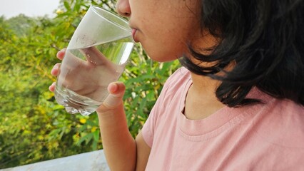 Fototapeta premium East Asian girl drink a glass of pure water with natural background. Healthy life style concept.