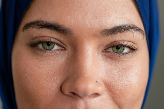 Indian woman showcasing green-hazel eyes with silver nose stud in studio with blue headscarf