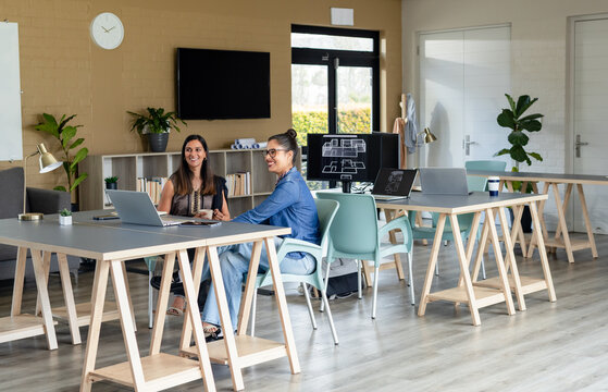 Diverse female colleagues reviewing floorplan designs on laptops and monitor in open office