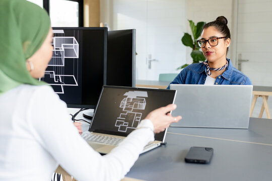 Diverse female colleagues reviewing floor plan schematic on laptops and phone in office, copy space