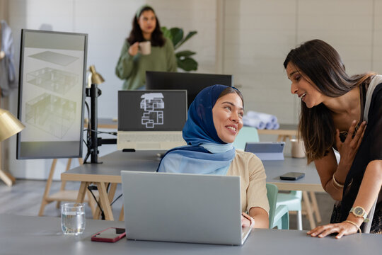 Diverse female coworkers collaborating over laptop and 3D architectural model monitor at office