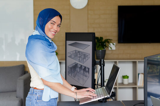 Indian adult woman typing on laptop at standing desk in open office with 3D architecture models