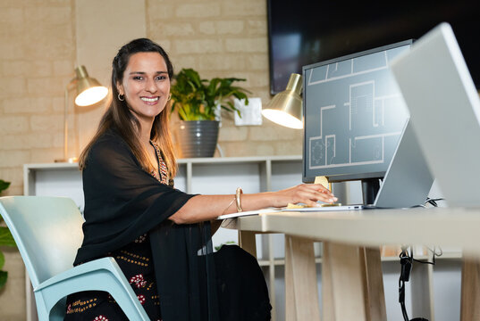 Indian woman typing on laptop in design studio with brass lamps floor plan monitor, copy space