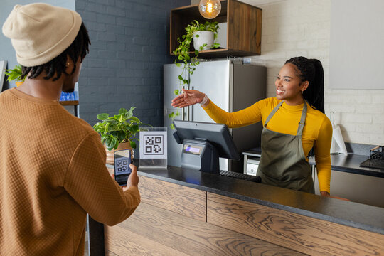 Hispanic barista greeting African American customer at cafe counter with card terminal, copy space