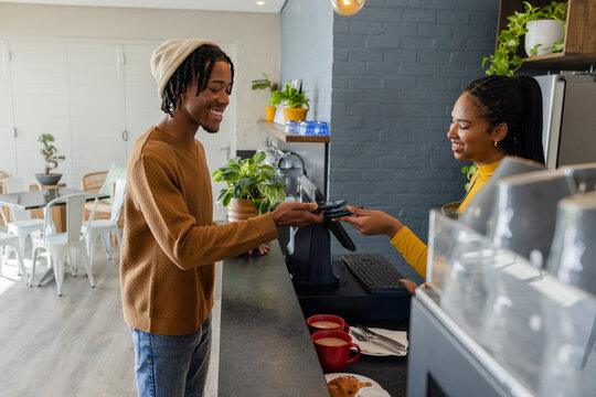 Diverse customer and cashier exchanging payment at cafe counter with red cups and pastries