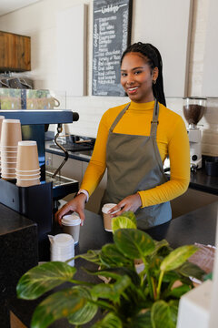 African American woman barista standing behind espresso machine in cafe holding two takeaway cups