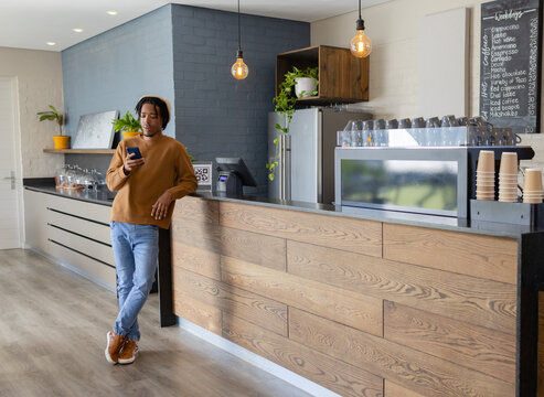 African American man leaning on counter with QR code and checking smartphone in cafe, copy space