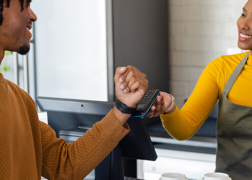 Female barista and African American male customer tapping smartwatch on reader at coffee counter