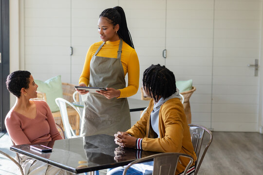 Diverse server and customers interacting while placing order on tablet and phone at cafe table